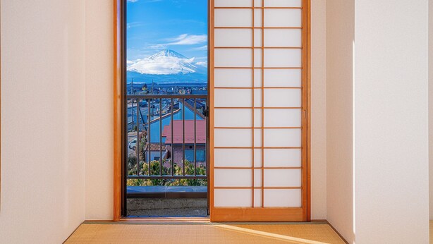 Een traditionele Japanse kamer met een schuifdeur die uitkomt op een balkon met uitzicht op een besneeuwde berg en een stadsgezicht.