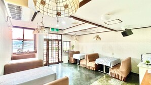 Een hotelkamer met een groot raam, een zithoek met tafels en stoelen, en een plafond met hanglampen.