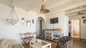 En kompakt opholdsstue med sofa, spisebord med stole, fjernsyn hængt på væggen og et tekøkken.