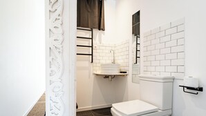 Et moderne badeværelse med hvide metrofliser, et hvidt toilet, et hvidt håndvaskspejl og en håndklæderække.