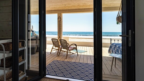 Strandudsigt fra en balkon med fletstole og et bord.