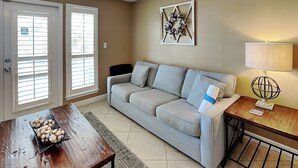 A living room with a grey sofa, a wooden coffee table with a basket of eggs, a lamp, and a wall decoration. - Grand Caribbean #309 West by Southern Vacation Rentals (Destin)