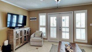 A living room with a television, a cabinet, a chair, a coffee table with decorative items, and a ceiling fan. - Grand Caribbean #309 West by Southern Vacation Rentals (Destin)