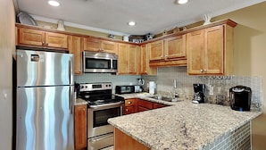 A modern kitchen with stainless steel appliances, wooden cabinets, and a granite countertop. - Grand Caribbean #309 West by Southern Vacation Rentals (Destin)
