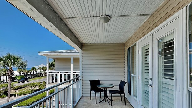 A balcony with a table and chairs, a view of the street, and a building with a white exterior. - Grand Caribbean #309 West by Southern Vacation Rentals (Destin)