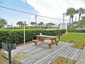 A wooden deck with picnic tables, surrounded by well-maintained hedges and palm trees. - Grand Caribbean #309 West by Southern Vacation Rentals (Destin)
