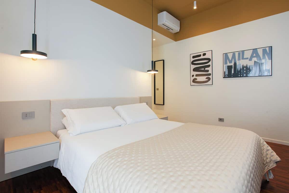 Une chambre à coucher comprenant un lit, une table de chevet, un climatiseur fixé au mur et deux tableaux encadrés.