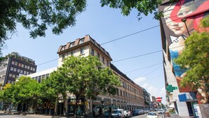 Vista de la calle con un edificio que tiene un letrero de McDonald's, coches estacionados y un gran mural a la derecha.