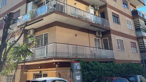 Un immeuble résidentiel à plusieurs étages, doté de balcons, de climatiseurs et d’un espace de stationnement avec des voitures.