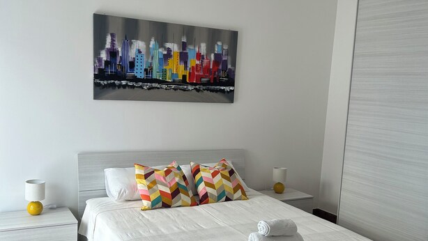Une chambre d’hôtel moderne avec un grand lit, un tableau représentant un paysage urbain et un plancher en bois.