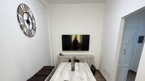 Un coin repas comprenant une table en bois, des chaises noires, un banc, une horloge murale et un téléviseur à écran plat.