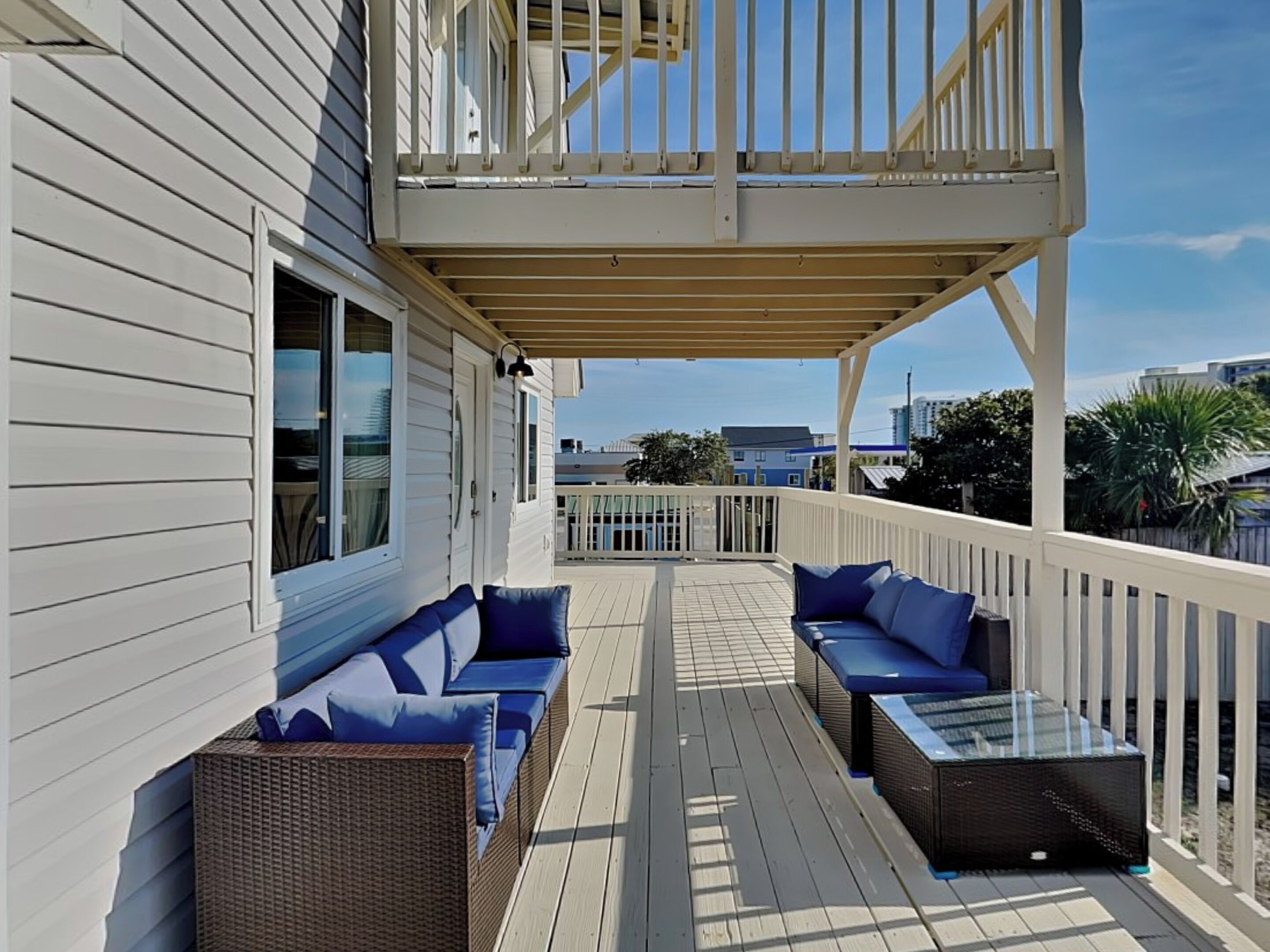 A covered deck with two sofas and a table, overlooking a residential area.