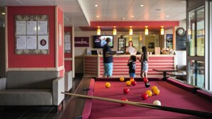 Een pooltafel met ballen, een zithoek en een bar met mensen op de achtergrond.