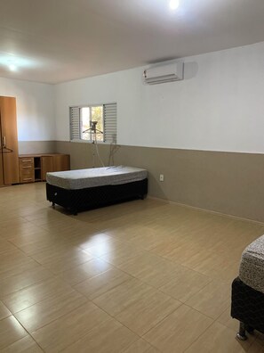 Una habitación con cama, armario, ventana con persianas, unidad de aire acondicionado y suelo de baldosas.