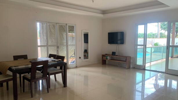 A spacious living room with a dining area, a flat-screen TV mounted on the wall, and a sliding glass door leading to an outdoor area. - Spacious 3-bedroom house in lovely Jardim Botanico with WiFi, AC (jardim botanico)