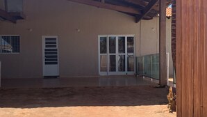A covered patio area with stone flooring, a palm tree, and a building with a tiled roof and glass doors. - Spacious 3-bedroom house in lovely Jardim Botanico with WiFi, AC (jardim botanico)