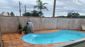 A swimming pool with a stone waterfall feature, surrounded by a concrete wall and potted plants. - Spacious 3-bedroom house in lovely Jardim Botanico with WiFi, AC (jardim botanico)