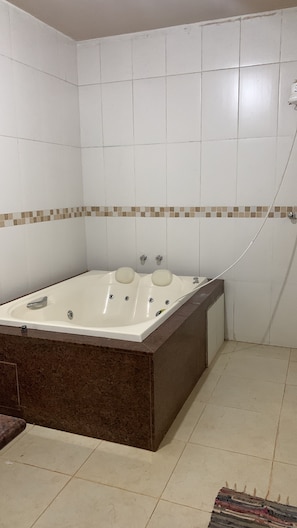 Un baño con una bañera grande, paredes y piso con azulejos.