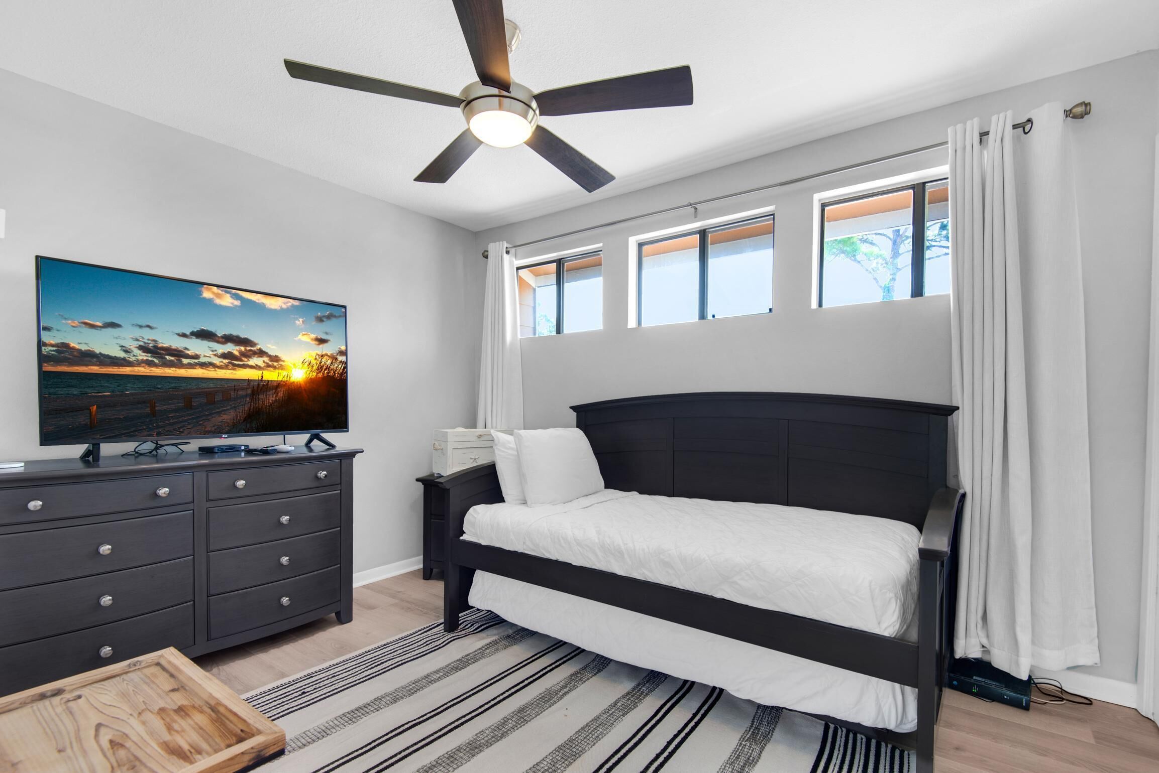 A bedroom with a bed, a TV, a dresser, and a ceiling fan.
