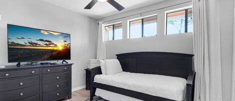A bedroom with a bed, a TV, a dresser, and a ceiling fan.