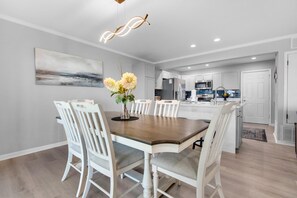Uma cozinha moderna com armários brancos, uma ilha central e um espaço de refeições com mesa de madeira e cadeiras brancas.
