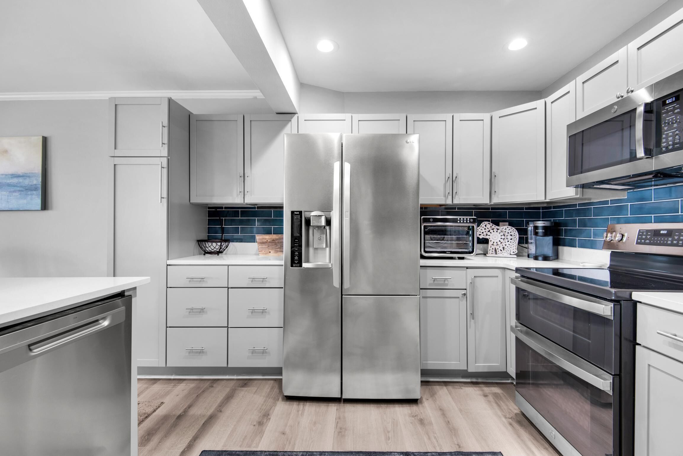 A modern kitchen with stainless steel appliances, white cabinets, and a blue backsplash.