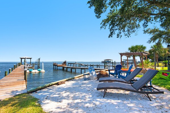 A beachside area with a wooden pier extending into the water, lounge chairs, and a gazebo.