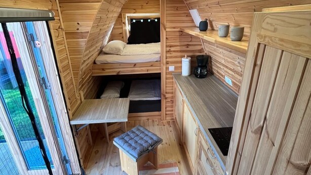 Un dormitorio acogedor en el ático con una cama litera, una mesita pequeña, un banco y una cafetera.
