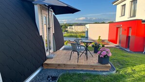 Una casa moderna con techo negro, terraza de madera y un pequeño patio con mesa y sillas.