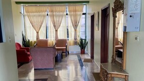 A hallway with a marble floor, a red sofa, a beige sofa, and a wooden table with a mirror. - Hostal la Colina (Tena)