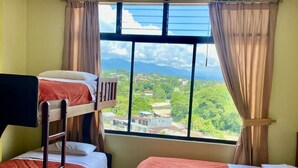 A room with bunk beds and a large window offering a view of a green landscape and buildings. - Hostal la Colina (Tena)