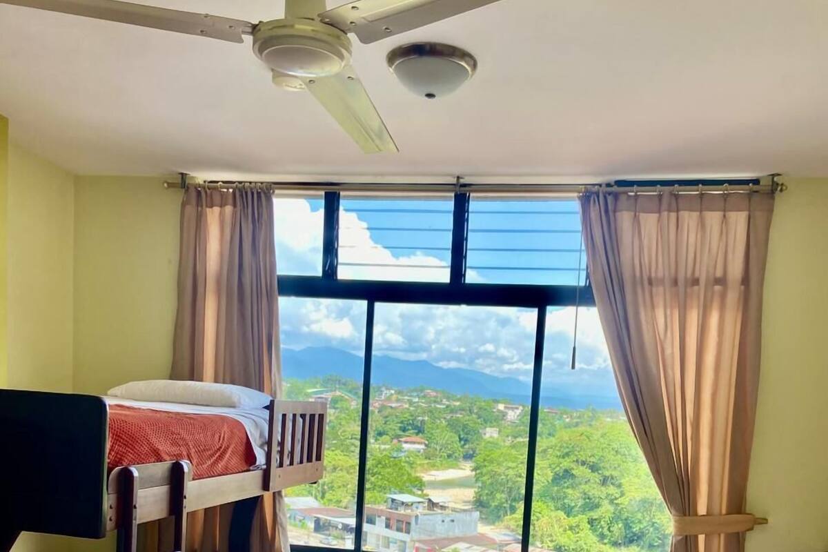 A room with bunk beds and a large window offering a view of a green landscape and buildings.