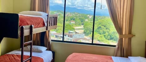Una habitación con literas y un amplio ventanal que ofrece vistas a un paisaje verde y edificios.