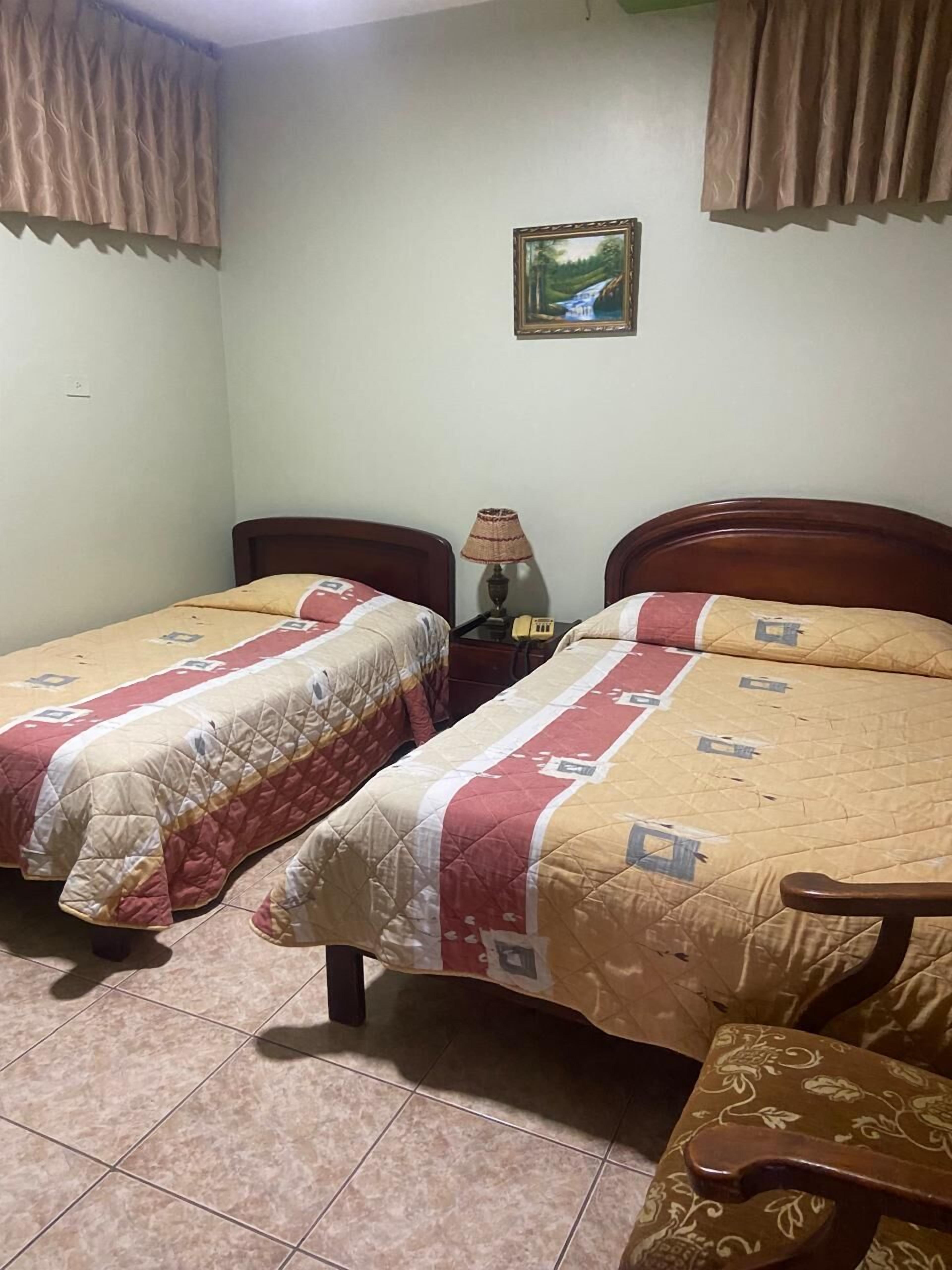 Ein Zimmer mit zwei Betten, einem Nachttisch mit Lampe und einem gerahmten Bild an der Wand.