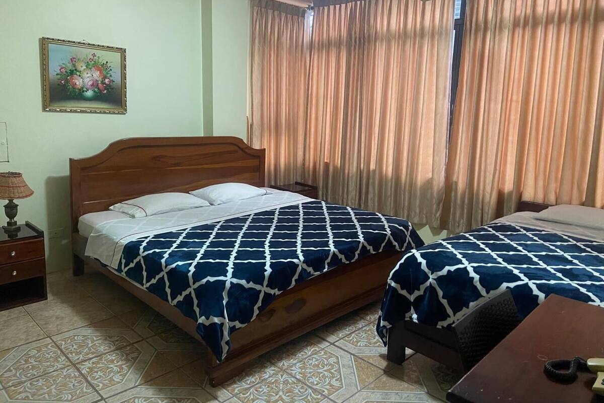 A hotel room with two beds, a wooden headboard, a nightstand with a lamp, and a painting on the wall.