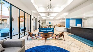 A modern hotel lobby with a blue sofa, a reception desk, and a pool view. - Signature Indio I-10 Coachella Valley by Sonesta (Indio)