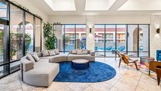 A spacious lobby with a large sectional sofa, a round coffee table, and a view of the pool area through large windows. - Signature Indio I-10 Coachella Valley by Sonesta (Indio)