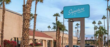 A hotel entrance with a sign for Signature Inn by Sonesta, palm trees, and parked cars.