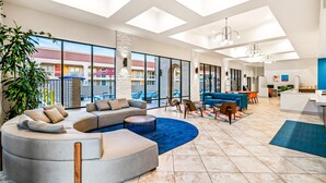 A spacious living area with a large sectional sofa, a round coffee table, and a dining area with chairs and a table. - Signature Indio I-10 Coachella Valley by Sonesta (Indio)