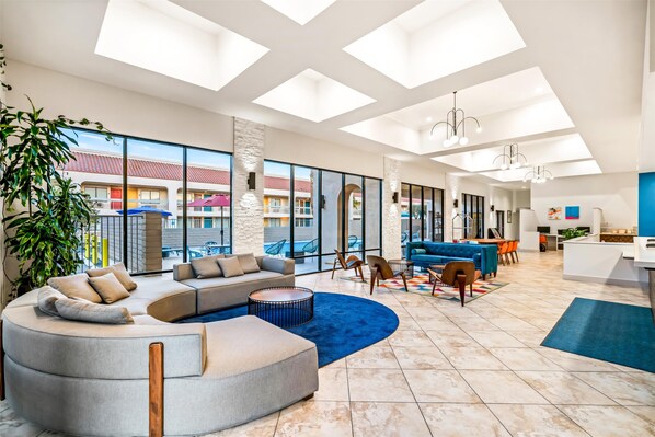 A spacious living area with a large sectional sofa, a round coffee table, and a dining area with chairs and a table. - Signature Indio I-10 Coachella Valley by Sonesta (Indio)