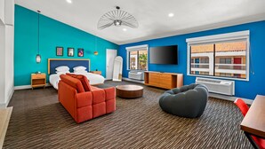 A modern hotel room with a teal accent wall, a large bed, a TV, a desk, and a window with a view of the outside. - Signature Indio I-10 Coachella Valley by Sonesta (Indio)