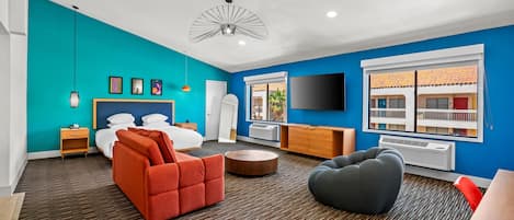 Quarto de hotel moderno com uma parede em tom de verde-água, uma cama grande, uma TV, uma escrivaninha e uma janela com vista para o exterior.
