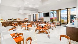 A modern restaurant with white walls, large windows, and orange chairs. - Signature Indio I-10 Coachella Valley by Sonesta (Indio)