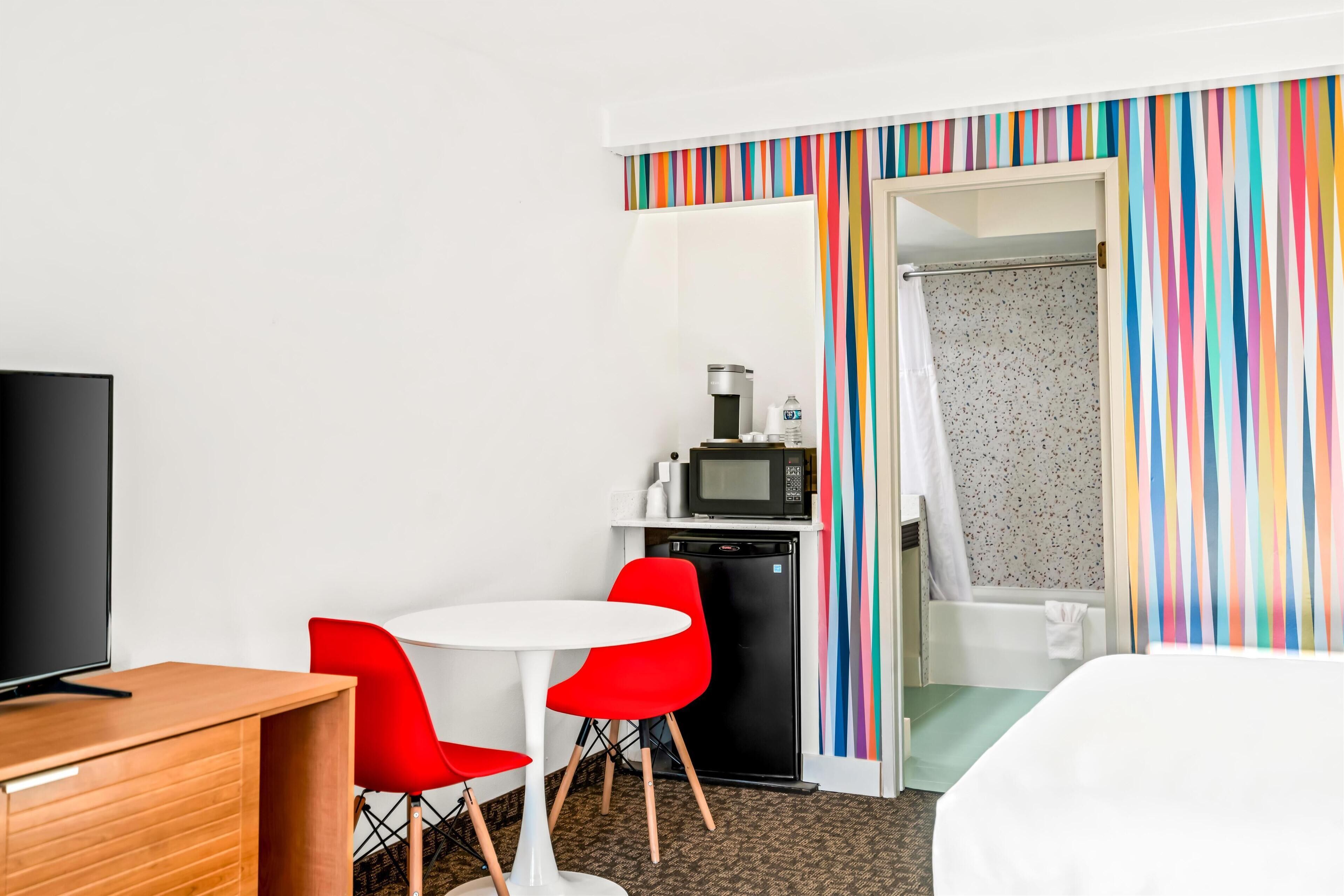 A hotel room with a bed, a TV, a small kitchenette, and a shower area.