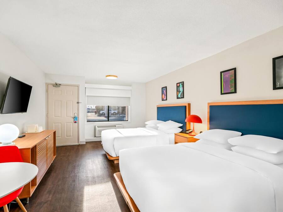 A hotel room with two beds, a desk, a chair, a TV, and a window with a view of the street.