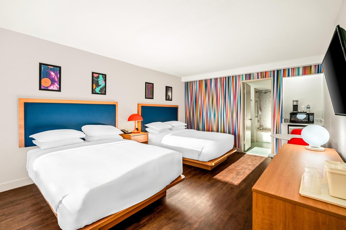 A hotel room with two beds, a wooden desk, a TV, and a bathroom visible through an open door.