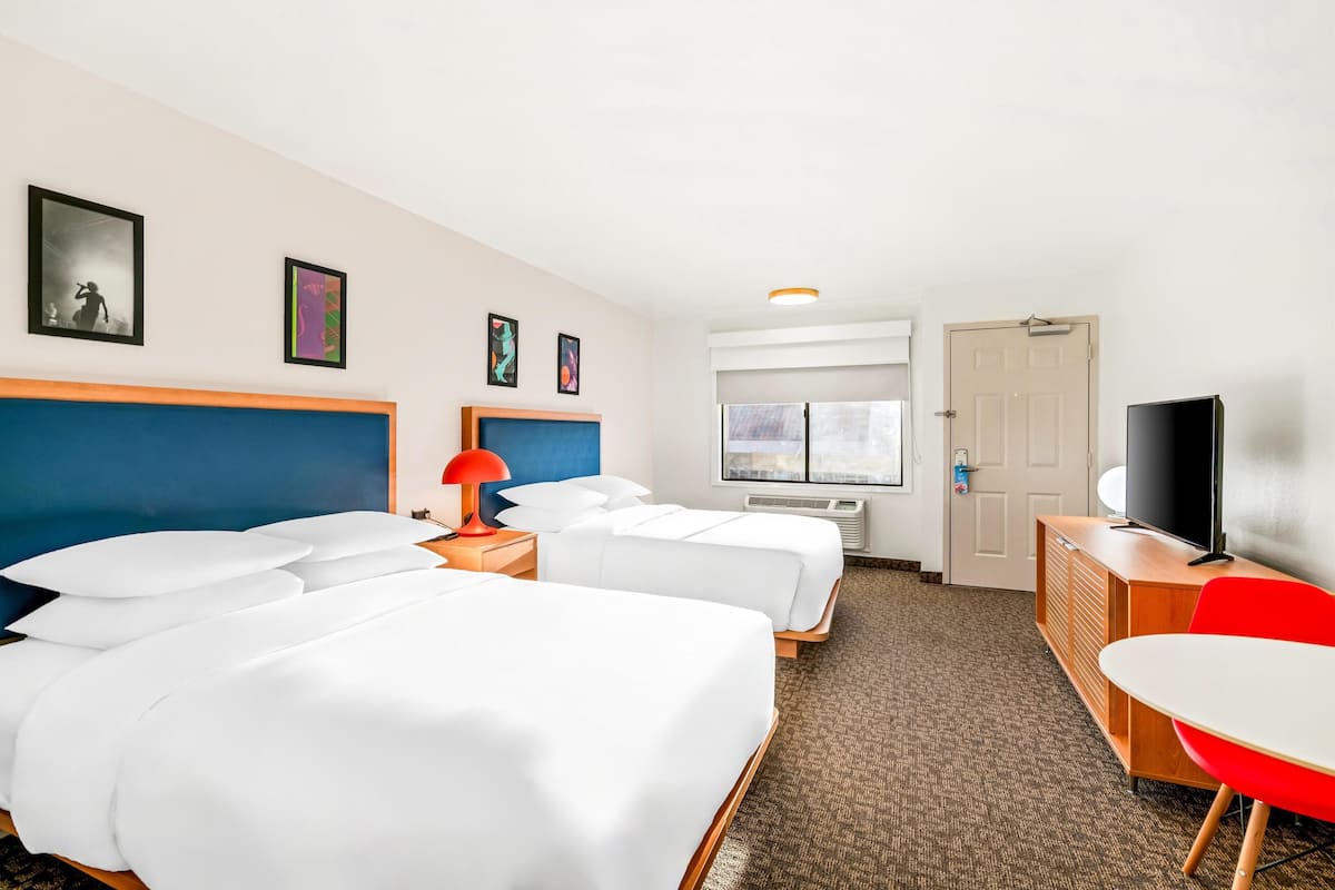 A hotel room with two beds, a TV, a desk, and a chair.