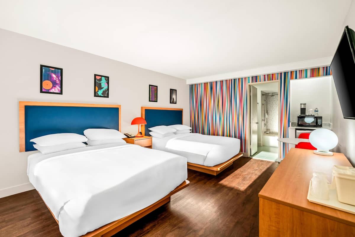 A hotel room with two beds, a wooden desk, a TV, and a bathroom visible through an open door.