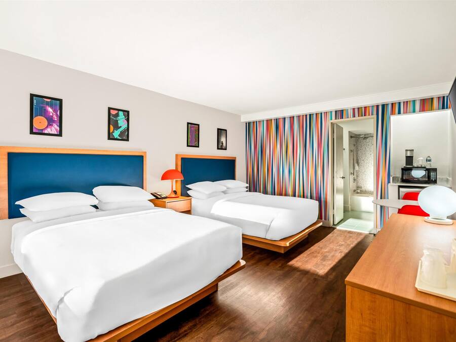 A hotel room with two beds, a wooden desk, a TV, and a bathroom visible through an open door.