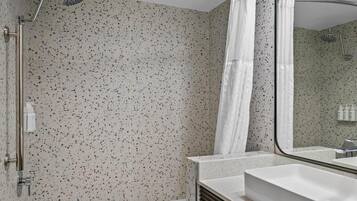 A modern bathroom with a freestanding bathtub, a shower with a handheld showerhead, and a large mirror.